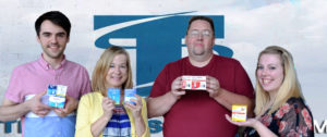 Four people holding boxes of diabetic test strips in front of logo